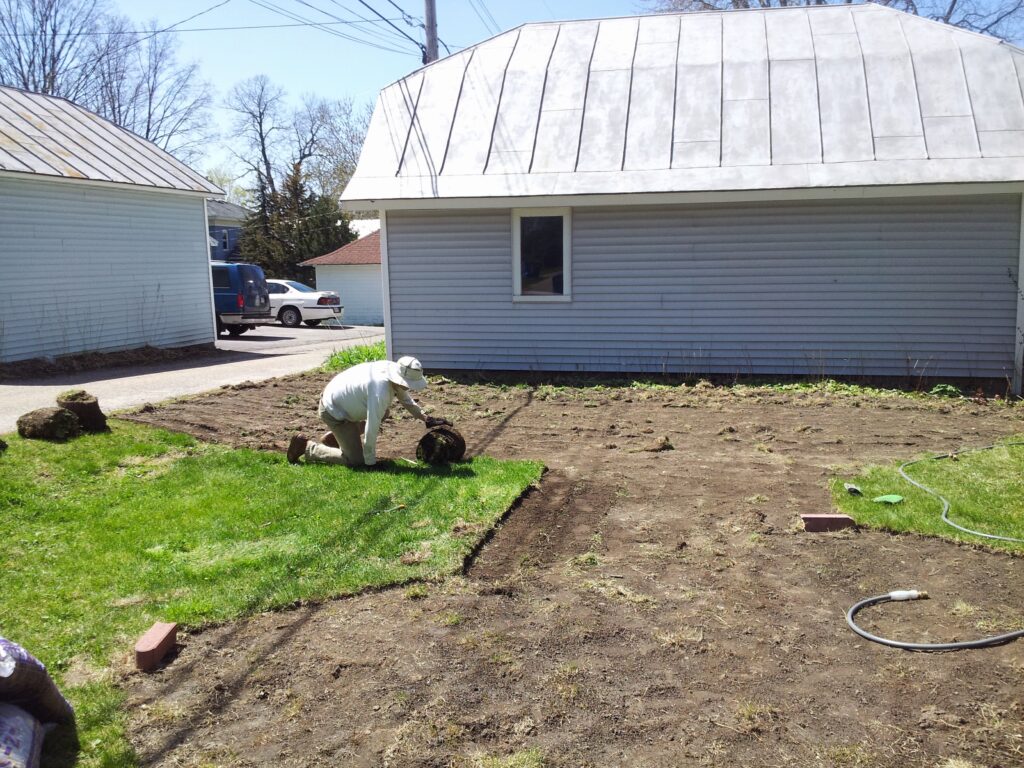 Neil rolling up sod in a backyard